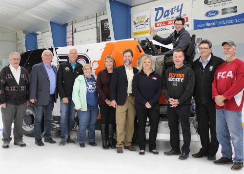 They unveiled the new Engo Wolf electric ice resurfacer at Frontenac Arena Friday evening with the mystery sponsor turning out to be the Frontenac Flyers. Pictured from left: arena board members and South Frontenac Council members Norm Roberts and Ray Leonard, South Frontenac Mayor Ron Vandewal, Central Frontenac Mayor Frances Smith, board member and Central Frontenac Coun. Sherry Whan, Lanark-Frontenac-Kingston MP Scott Reid, Frontenac Fury President Lynn Newton, Frontenac Flyers President Al Pixley, board member and Central Frontenac Coun. Brent Cameron and Jim Stinson, who drove the resurfacer onto the ice for the first time. Arena Manager Tim Laprade is in the driver’s seat of the resurfacer. Photo/Craig Bakay